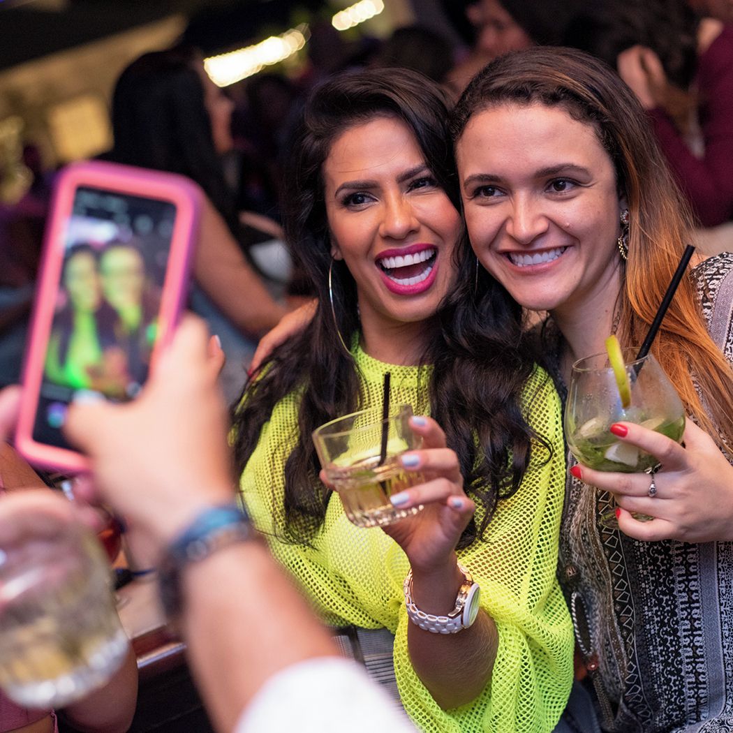 Two women smiling and holding cocktails at Blue Martini, captured during a lively club night.